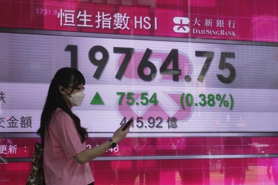 A woman wearing a face mask walks past a bank's electronic board showing the Hong Kong share index in Hong Kong, Wednesday, Aug. 3, 2022.