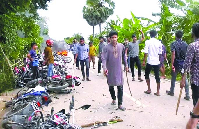 A group of youth with sticks is seen next to vandalised motorcycles at C&B area of Barguna's Patharghata upazila on Sunday afternoon.