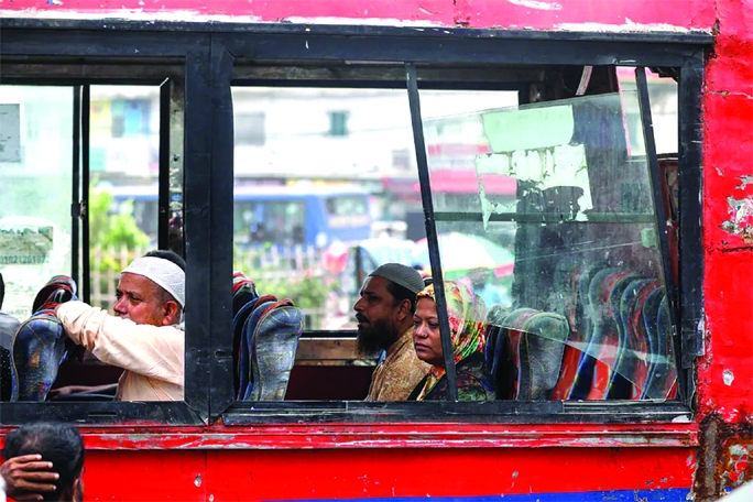 Passengers peek through a half-broken window, glass of a bus, they move their destination despite having risks in the city's Mohammadpur Beribandth intersection on Tuesday.
